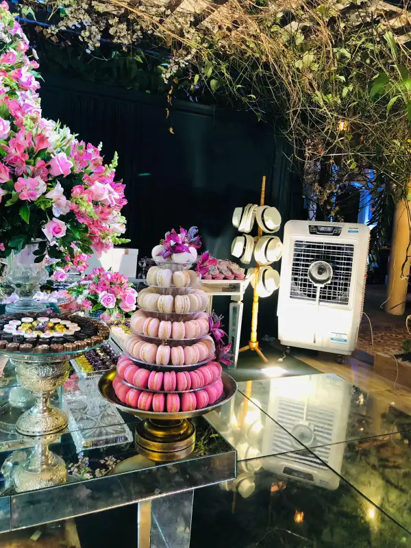 Climatizador da FG Climatizadores em funcionamento ao lado da mesa de doces de um evento, decorada com flores e uma torre de macarons